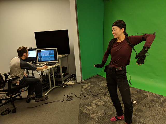 A woman wearing virtual reality technology dances next to a man on a computer
