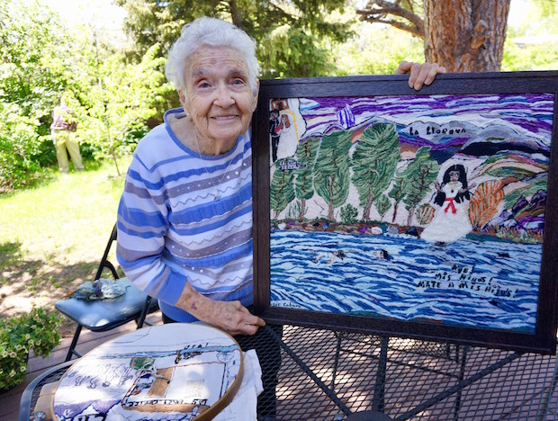 A woman standing next to an embroidered piece with a frame.