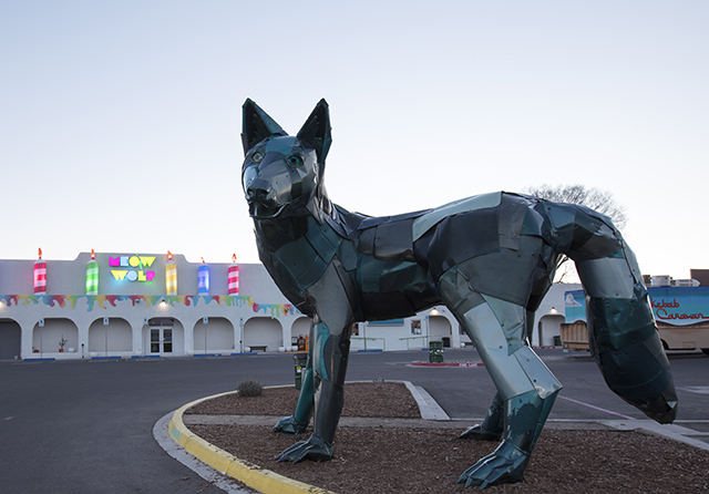 A sculpture of a coyote outside a building that says Meow Wolf and is decorated with giant birthday candles