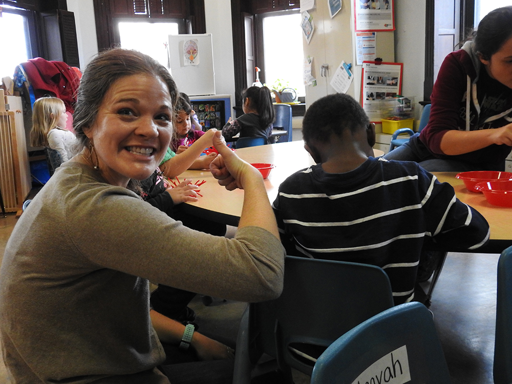 Woman arts teacher giving a thumbs up in a classroom full of students. 