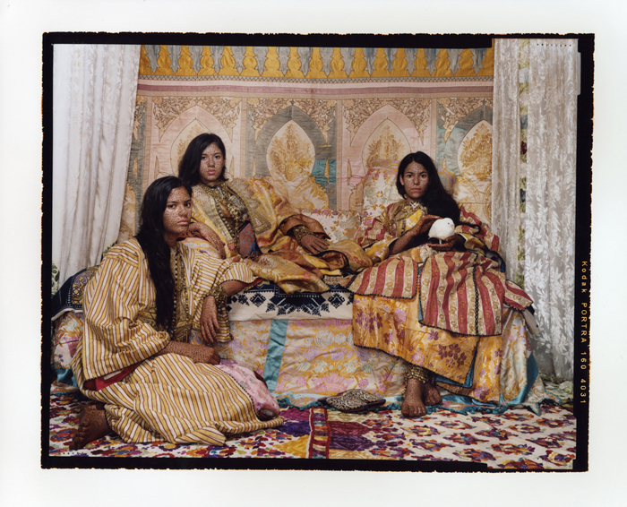Three women in colorful clothes with hena-colored bodies. 