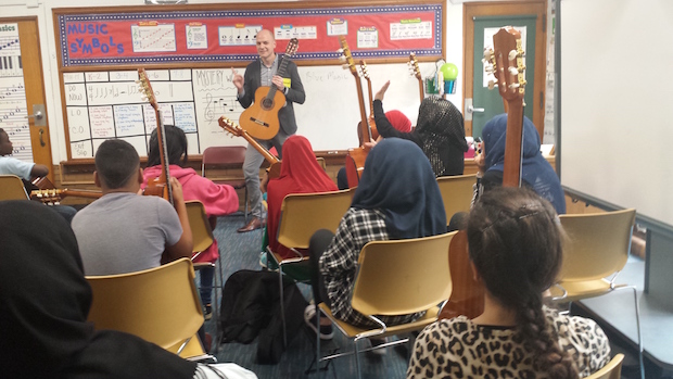 students in a classroom setting listening to a teacher who's standing in front of a board filled with music notation and terminology