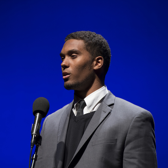 a young african-american man in a gray suit recites into a microphone