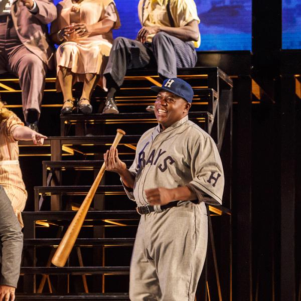 Man in baseball uniform holding a bat on stage. 