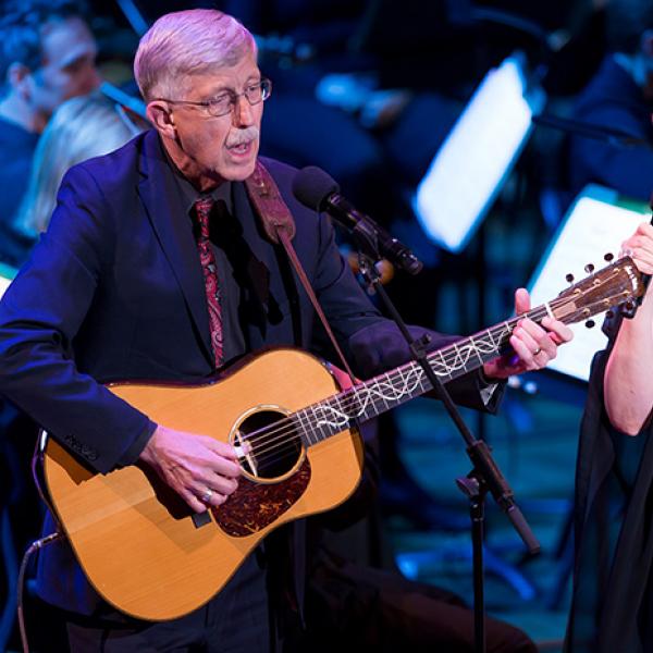 An older man playing a guitar next to a woman singing