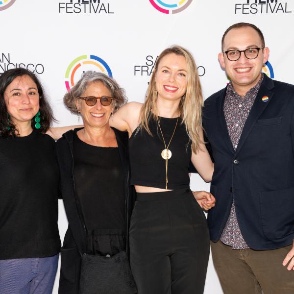 From left to right: three women and one man stand in front of a step-and-repeat that has “SAN FRANCISCO JEWISH FILM FESTIVAL” and “JFI” written in various places.