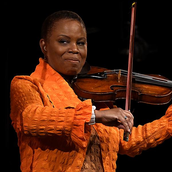 Black woman in orange jacket playing a violin.