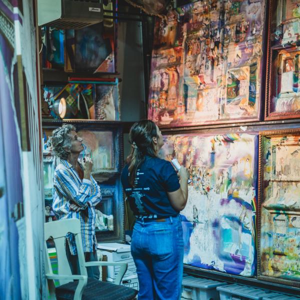 Two women standing and looking up at several large paintings.