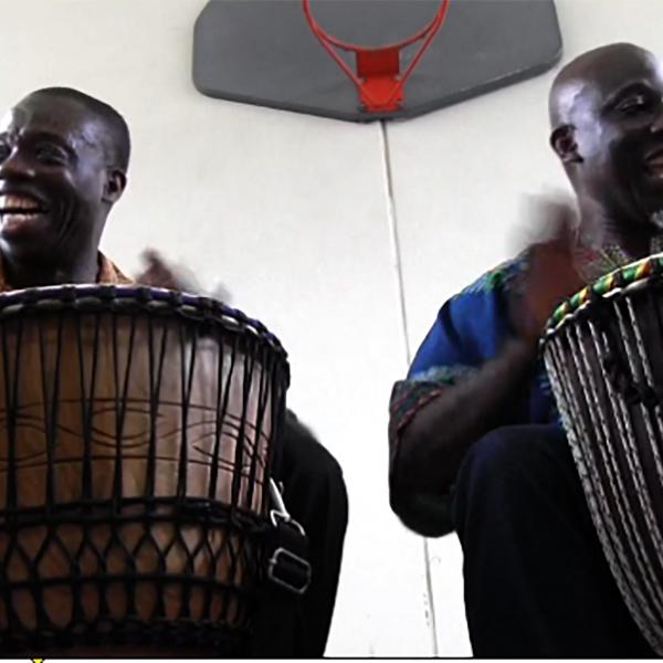 Two men playing drums in a gym. 