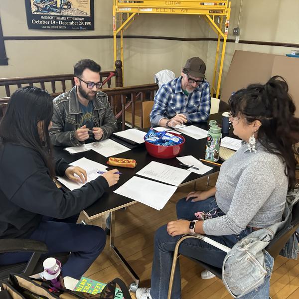 Two men and two women are seated together around a table with papers and pens.