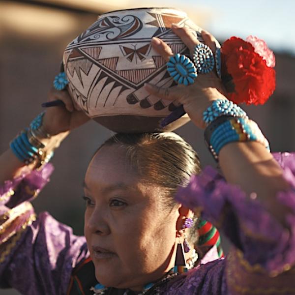 Native American woman holding a ceremonial pot on her head while moving forward