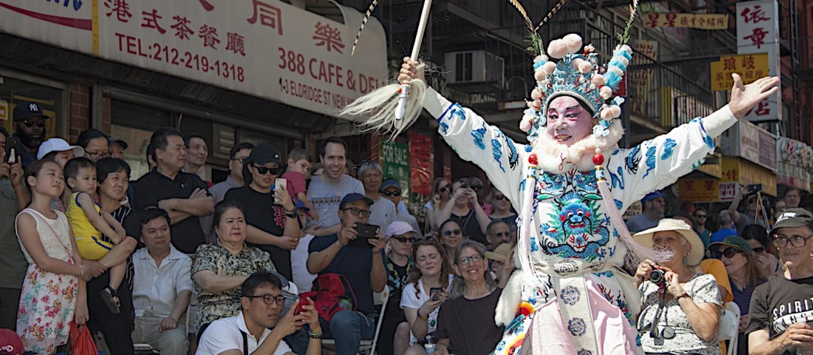 Elaborately costumed figure in parading down a city street surrounded by a large crowd