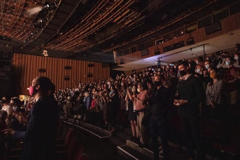 Rows of audience members wearing masks and sitting in a performing arts venue waiting for a performance. 