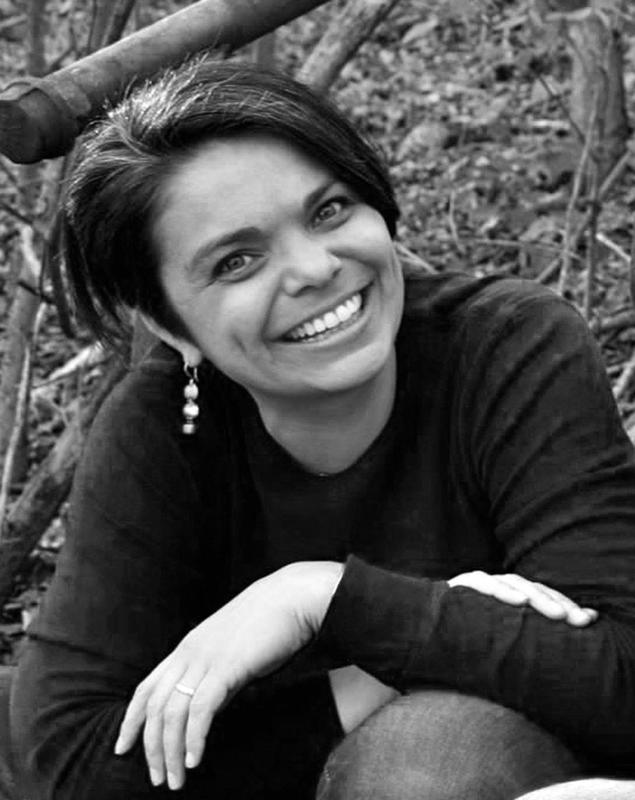 Woman with black hair wearing a dark long-sleeved shirt smiling and posing outdoors. 