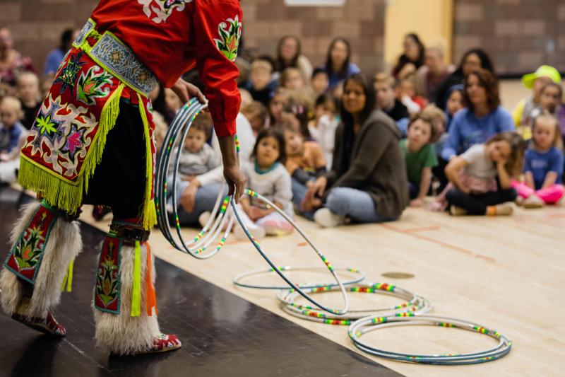 Native man holding several hula hoops in front a crowd of elementary school students and teachers. 