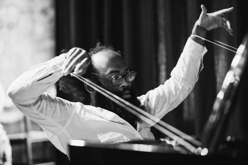 Black man with glasses conducting an orchestra. 