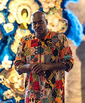 Man in a colorful outfit in front of a large fabric 
