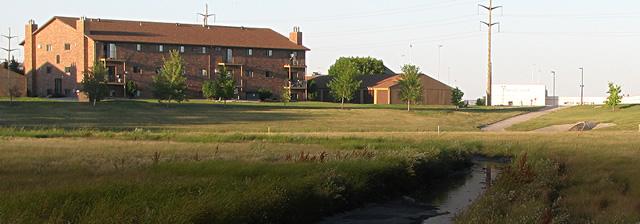 Grassy drainage basin field near rural structures