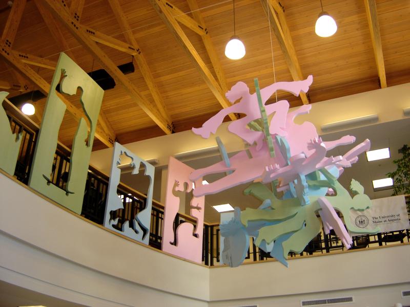 an installation in an atrium of Peter Buotte's People Puzzle, which comprises cut outs of people in various poses attached togehter, and surrouded by boards revealing the negative space left by the cutouts