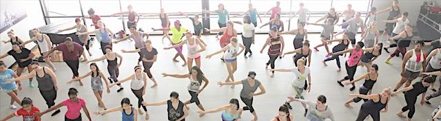 Large group dancing in an indoor performance space as seen from a balcony above