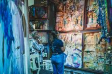 Two women standing and looking up at several large paintings.