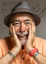 A man in a straw hat, with a broad smile, holding his head in his hands