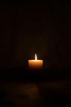 a single lit candle against a backdrop of darkness