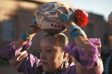 Native American woman holding a ceremonial pot on her head while moving forward