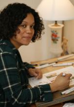 Cartoonist Whit Taylor sits at her drafting desk with marker in hand
