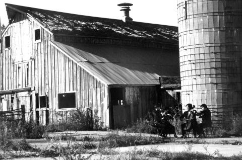 A string quartet playing in front of a barn and silo outdoors. 