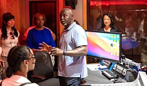 A man stands in a recording studio speaking to a group of individuals.