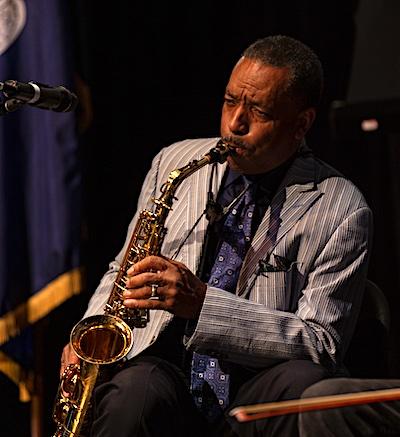 A man sits in a chair playing a saxophone
