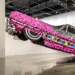 Life-size lowrider car piñata hanging in a museum