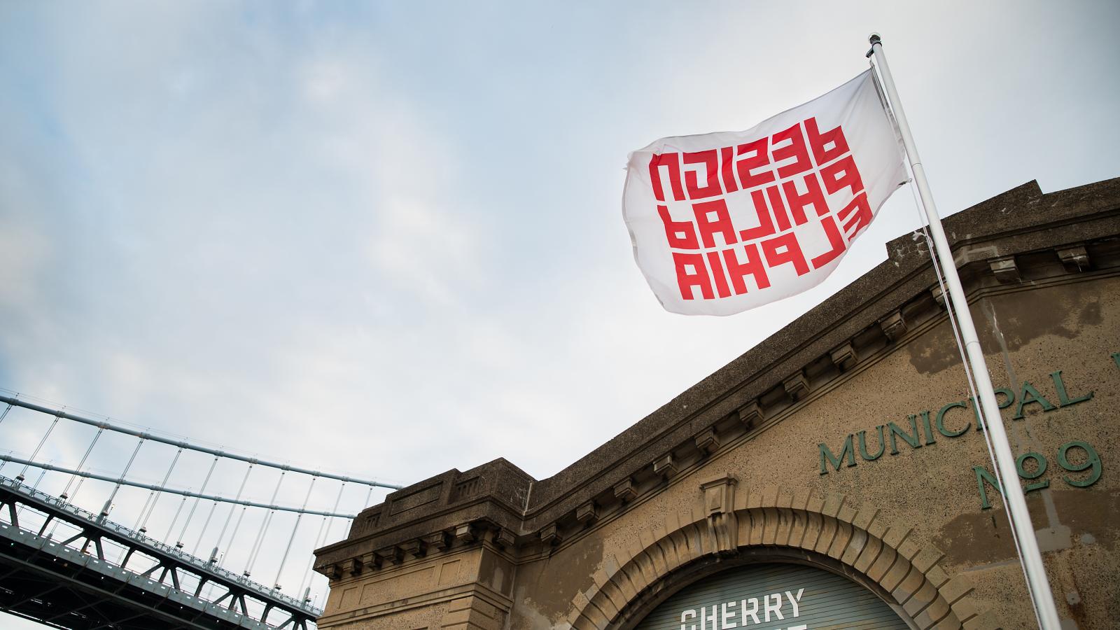 A large brick building with a flag waving outside it that says Design Philadelphia