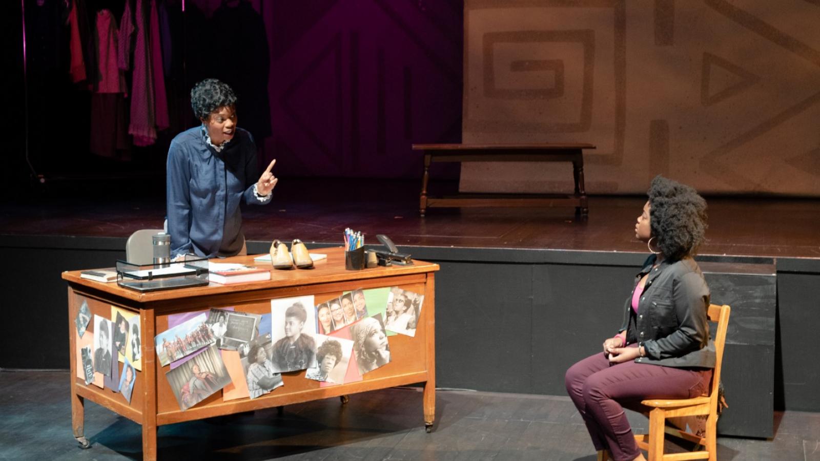 An actress plays the role of a teacher talking to a student from her desk