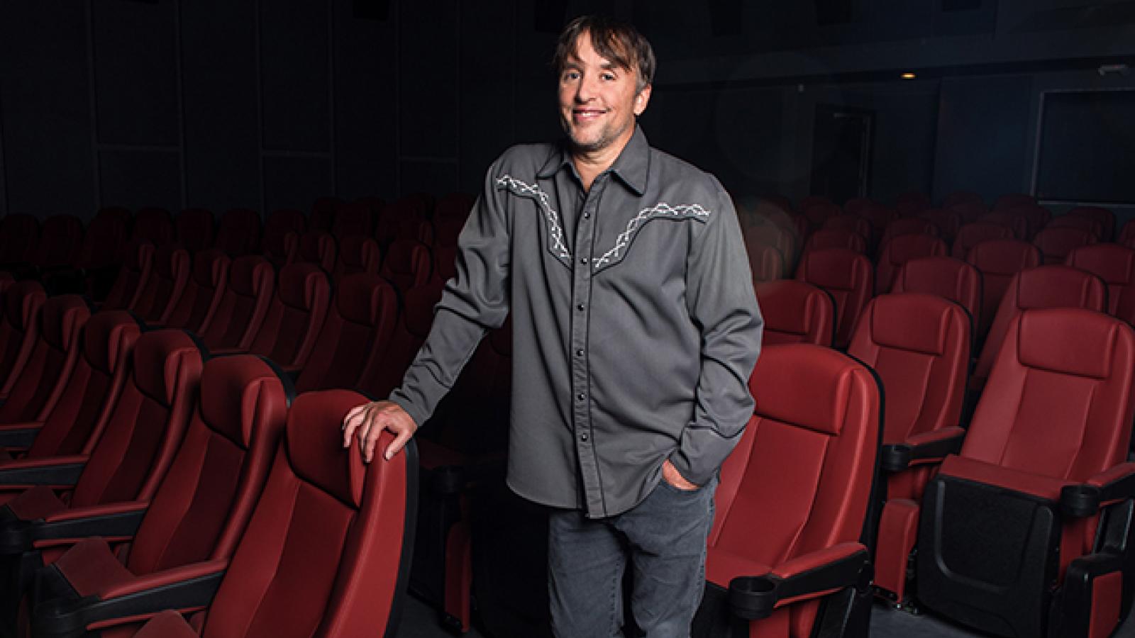 Man standing while holding onto red theater seats