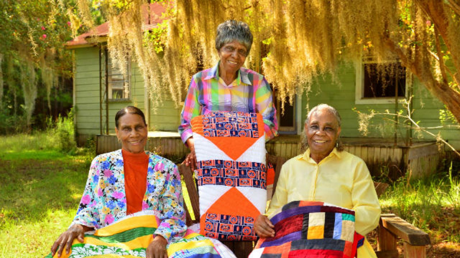 Three African-American women holding quilts