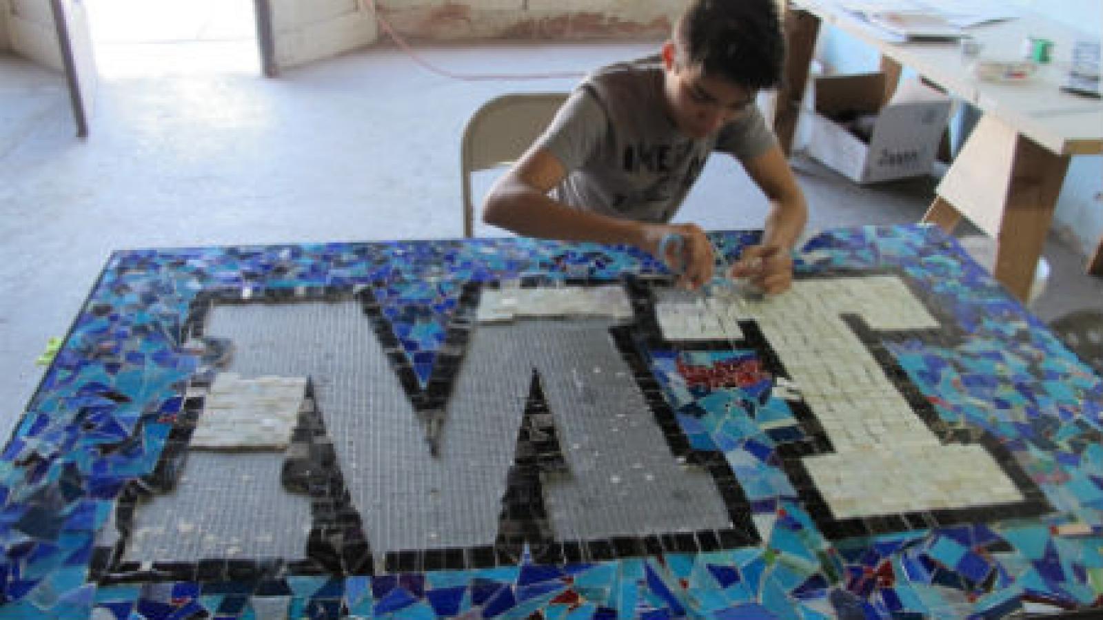 Boy at a table assembling a mosaic with the letters MT.