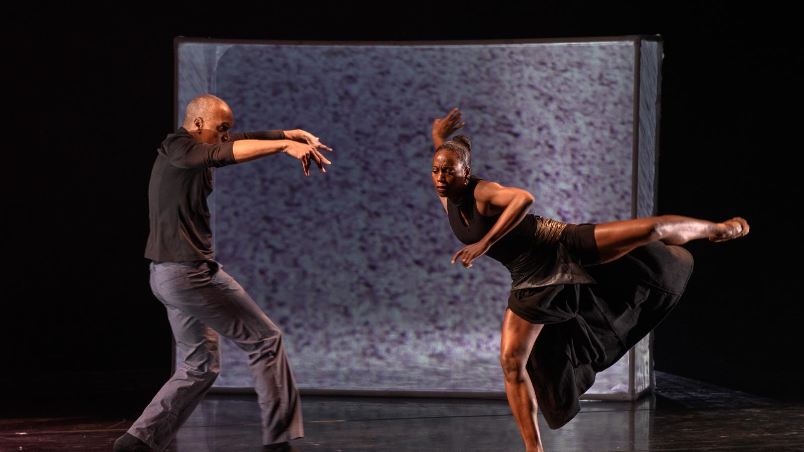 A Black man in tee-shirt and jeans dancing with a Black woman in a black dress. 