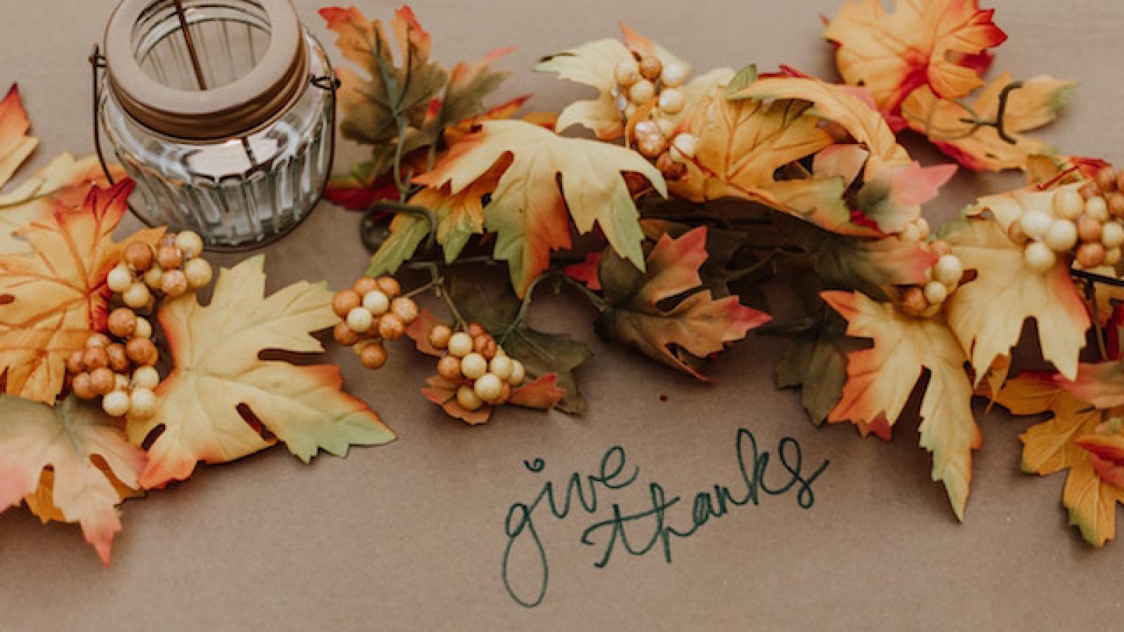 ribbon-like arrangement of fall leaves on a table with a votive candle and Give Thanks handwritten in script