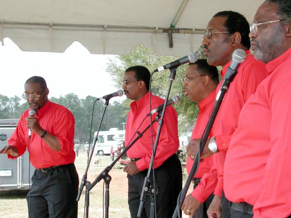 Five men wearing red shirts on stage singing. 