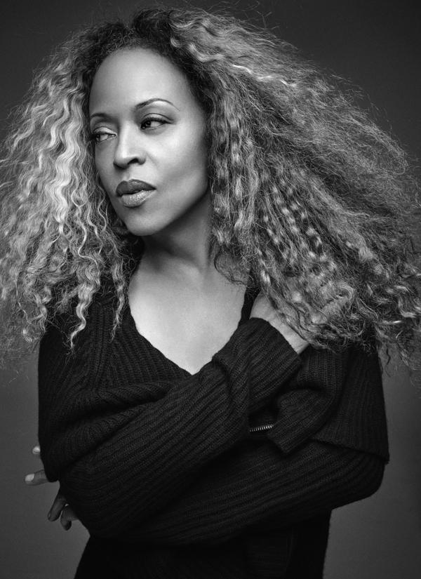 Portrait of Black woman with long, wavy hair looking away from the camera, wearing a black shirt. 