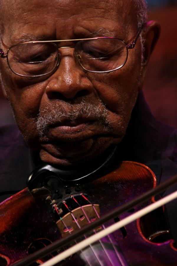 Elderly Black man wearing glasses playing a fiddle.