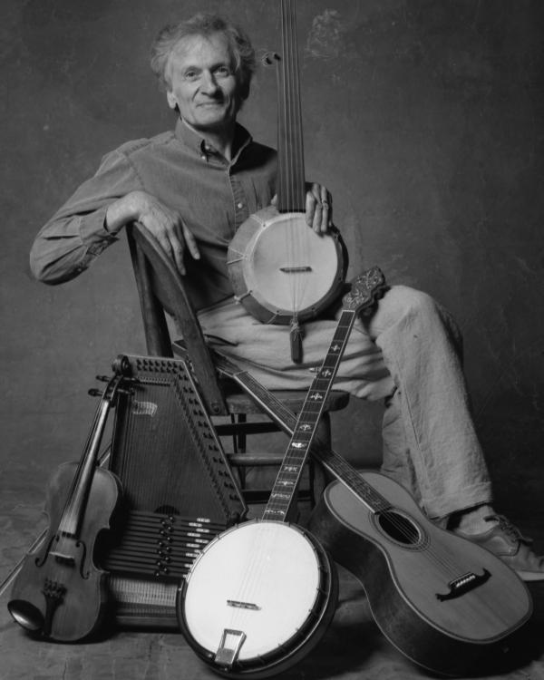 Man sitting in wood chair surrounded by string instruments. 