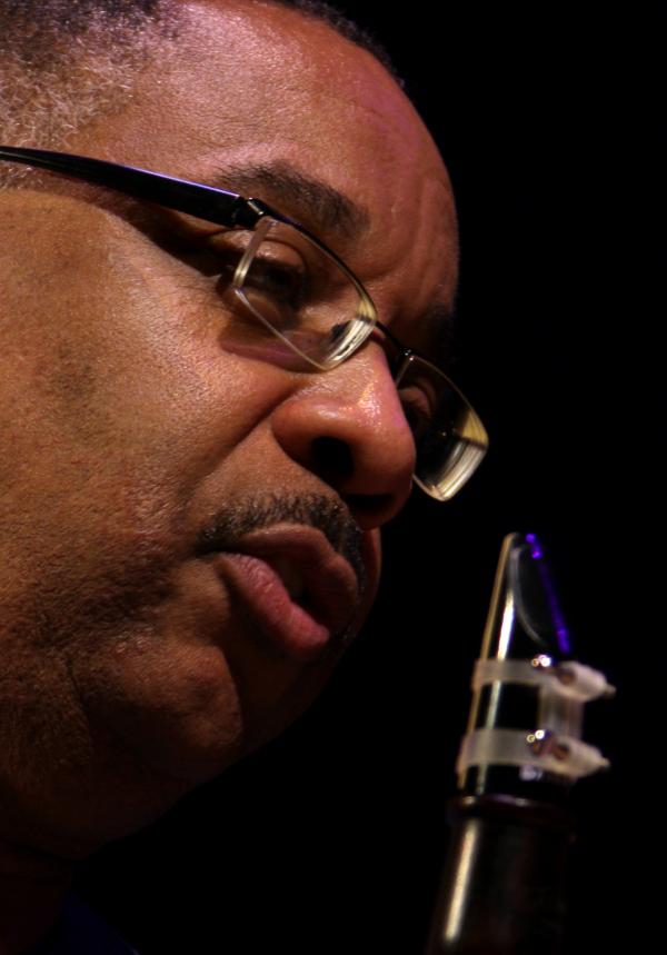 Older Black man wearing glasses holding a clarinet.