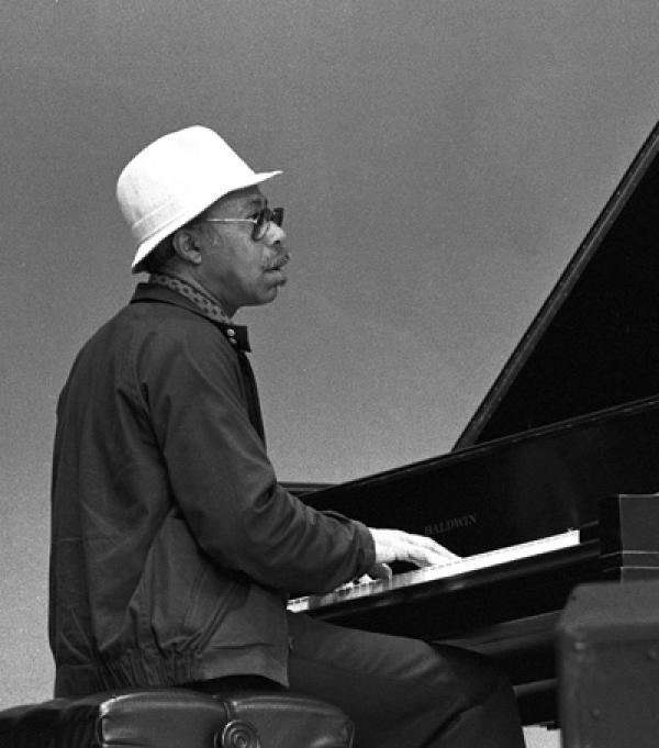 Man in white hat playing piano on stage. 